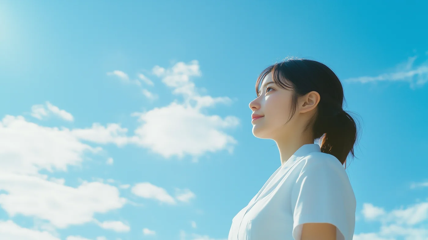 希望を見上げる女性医療従事者と青空。澄み渡る青空を見上げ、未来への希望に満ちた表情を浮かべる若い女性医療従事者の横顔です。明るく爽やかな印象を与えます。