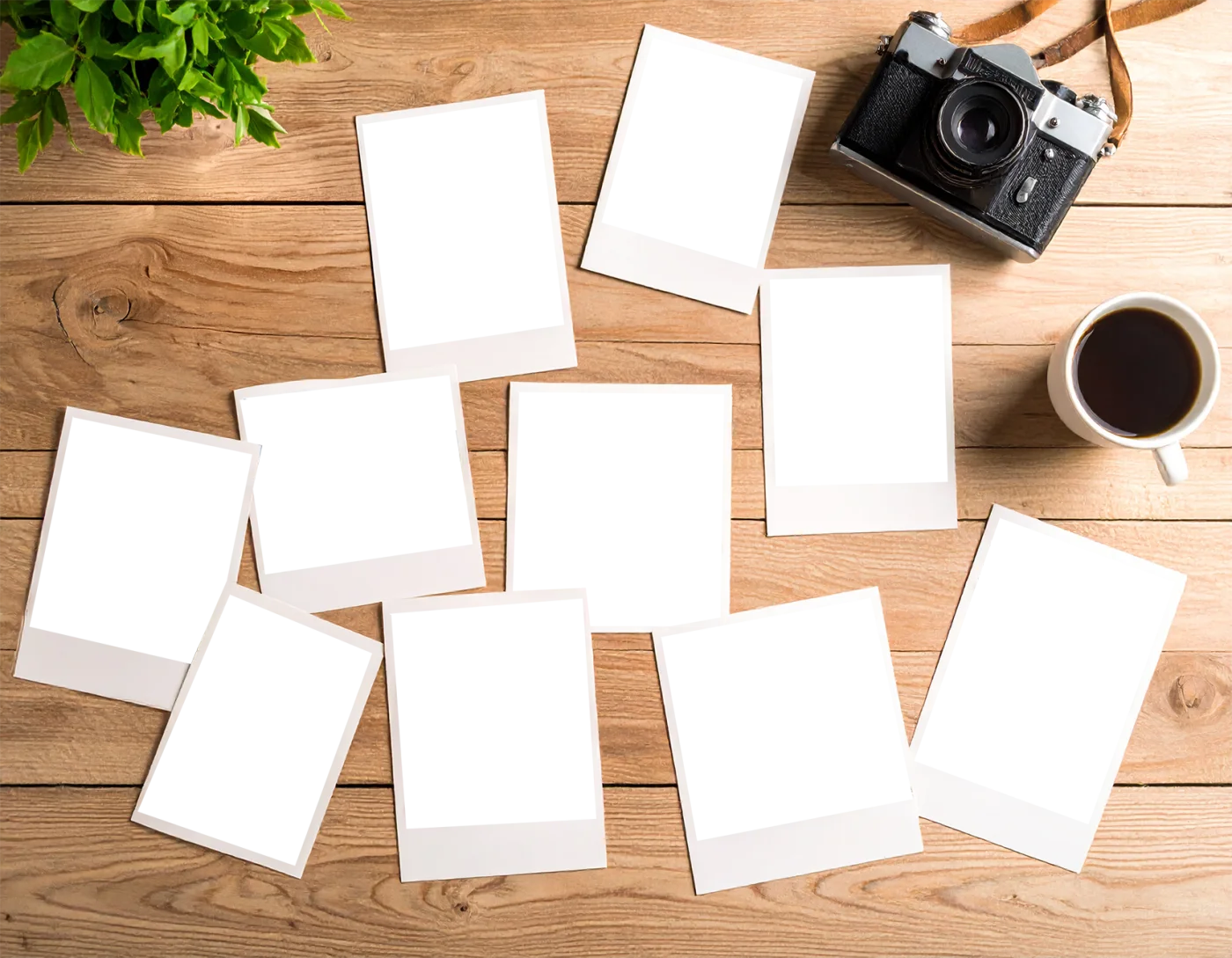 木製デスクに散らばるインスタント写真フレームとレトロカメラ、コーヒーの俯瞰
