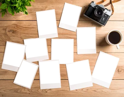 木製デスクに散らばるインスタント写真フレームとレトロカメラ、コーヒーの俯瞰